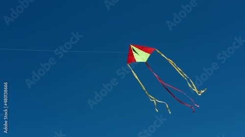 Red yellow kite fly high in blue cloudless sky. Slow motion