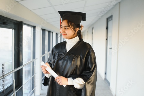 Happy Indian university student in graduation gown and cap holding diploma certificate.