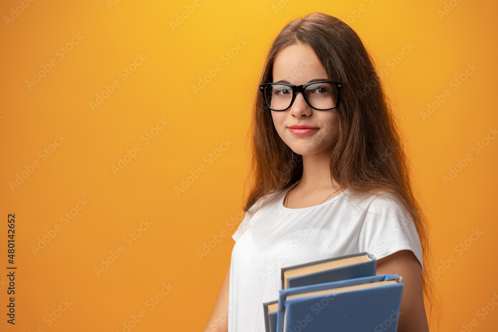 Smart teen girl in glasses holding book against yellow background Smart teen girl in glasses holding book against yellow background