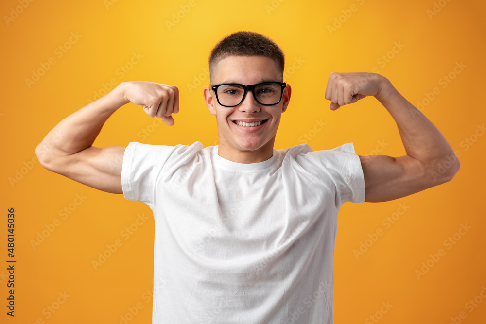 Caucasian muscular teenager boy shows his strength against yellow background Caucasian muscular teenager boy shows his strength against yellow background
