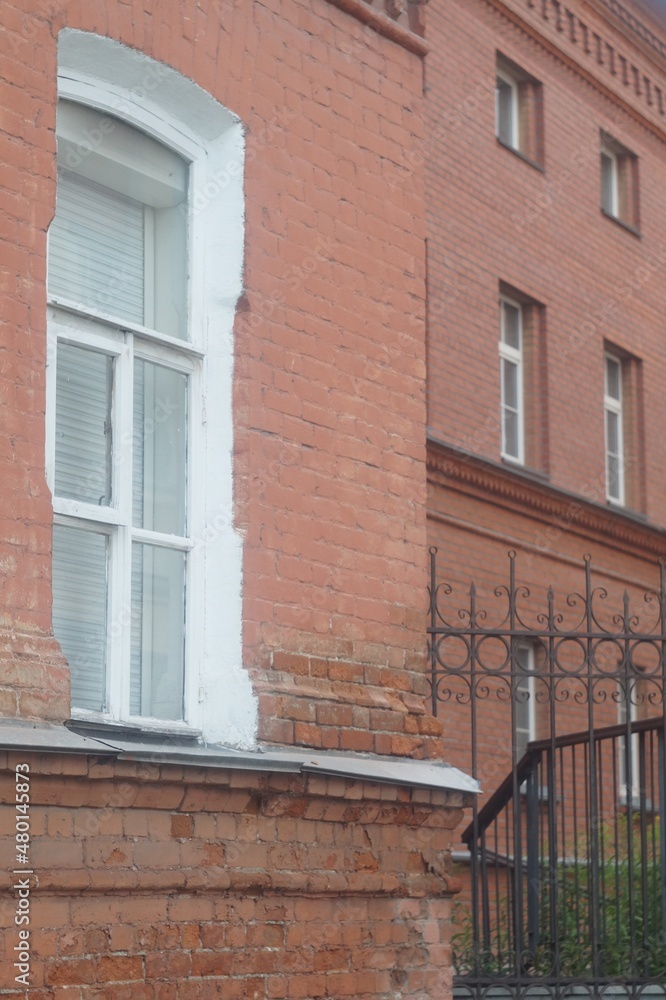 Full-color vertical photo. Part of the facade of an ancient building. In the frame there is a window and a wall of red brick masonry.