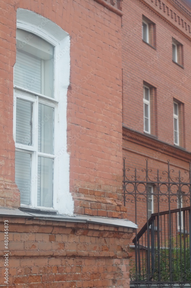 Full-color vertical photo. Part of the facade of an ancient building. In the frame there is a window and a wall of red brick masonry. Full-color vertical photo. Part of the facade of an ancient building. In the frame there is a window and a wall of red brick masonry.