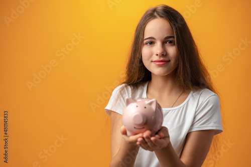 Teen girl with piggy bank on yellow background.