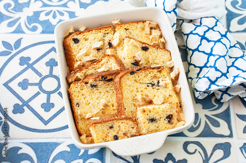 Bread (panettone) pudding from leftovers with custard and raisins in a baking dish on a blue background.