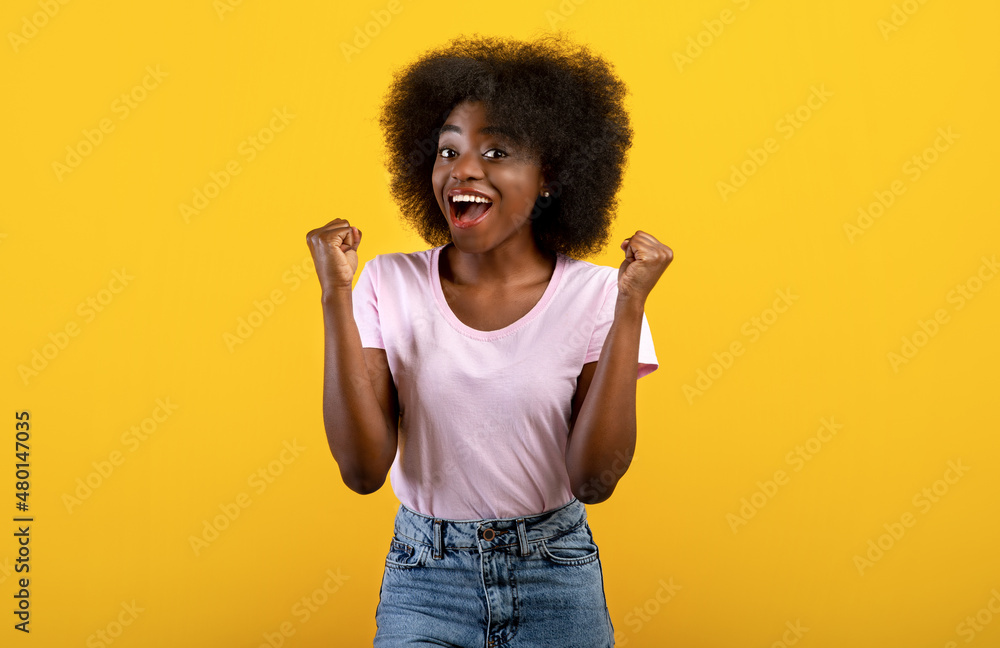 Positive african american lady gesturing YES, feeling excited and triumphant on yellow studio background