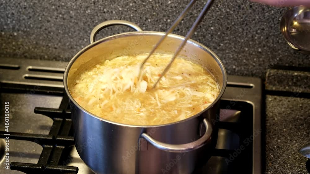 The cabbage is stirred into the broth with long metal tongs. Soup preparation. cabbage soup. Close-up The cabbage is stirred into the broth with long metal tongs. Soup preparation. cabbage soup. Close-up
