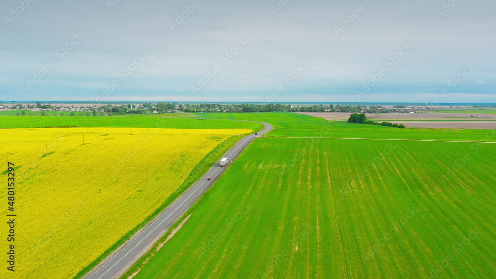 Obraz premium Aerial View Of Highway Road Through Field And Summer Wheat Fields Landscape. Top View Of Truck Tractor Unit Prime Mover Traction Unit In Motion On Freeway. Business Transportation, Trucking Industry