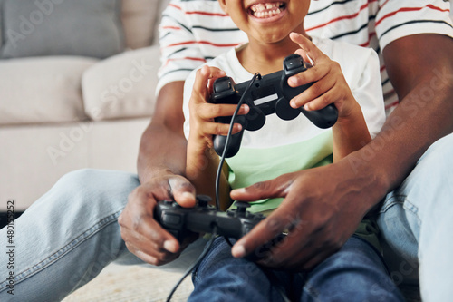 With joysticks in hands. African american father with his young son at home