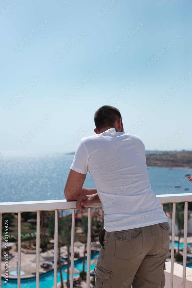 Tourist man standing in hotel terrace looking over the sea. Vacation lifestyle background.