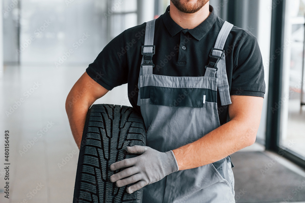 Holding tire. Man in uniform is working in the autosalon at daytime Holding tire. Man in uniform is working in the autosalon at daytime