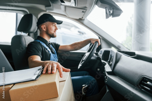 Modern vehicle. Delivery man in uniform is indoors with car and with order © standret