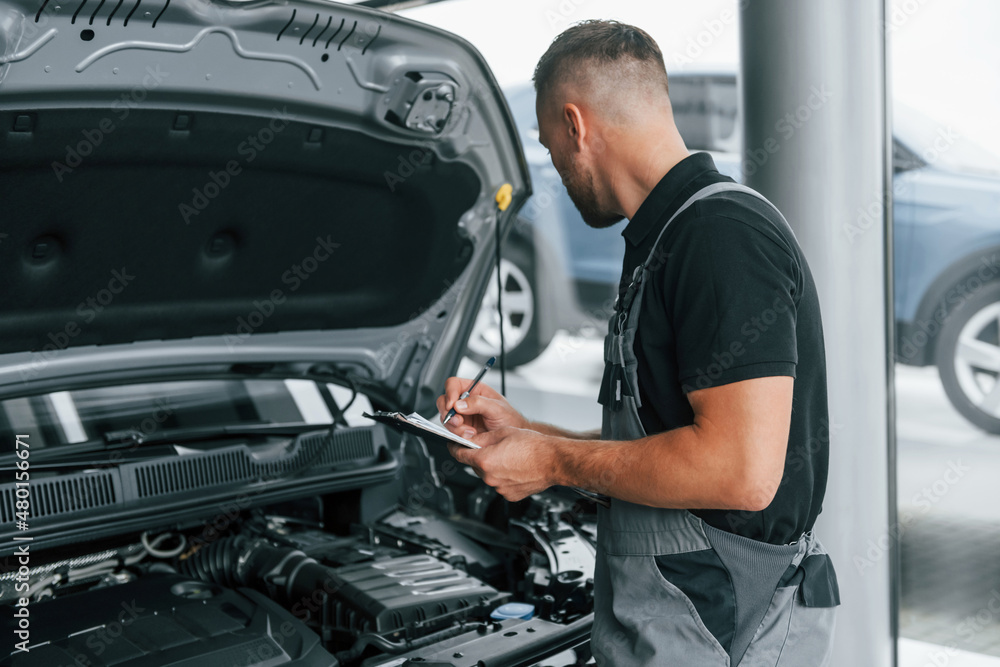 Under the hood. Man in uniform is working in the autosalon at daytime