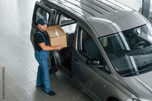 In blue colored clothes. Delivery man in uniform is indoors with car and with order © standret