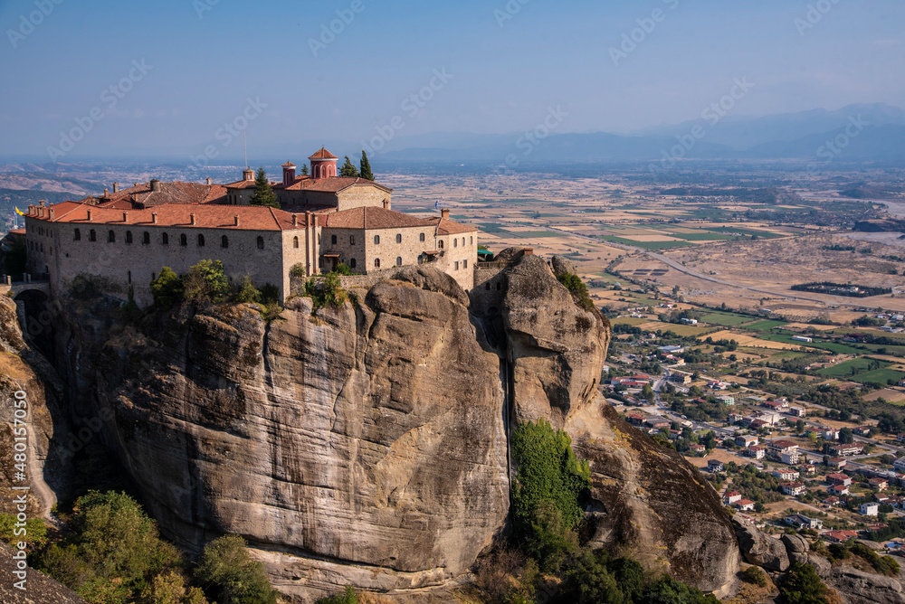 Beautiful scenic view of Orthodox Monastery of Áyios Stéfanos (St. Stephen) on cliff, immense monolithic pillar, at the background of stone wall and rock formations of Meteora mountain, Greece.