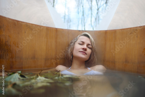 A young woman takes hot bath in oak barrel in the winter outside. Steam barrel and spa center.