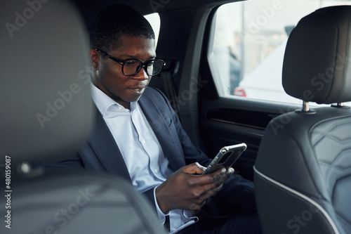 In glasses. Young african american businessman in black suit is in the automobile © standret