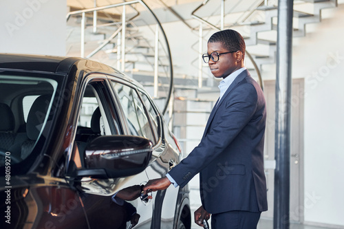 Opening the door. Young african american businessman in black suit is the autosalon © standret