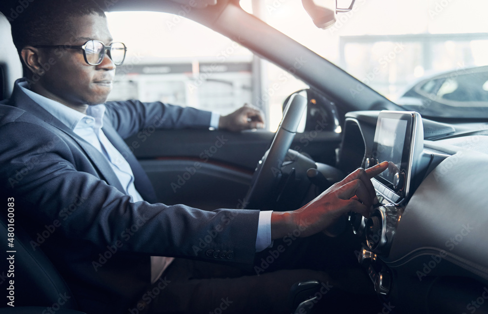Using front control panel. Young african american businessman in black suit is in the automobile Using front control panel. Young african american businessman in black suit is in the automobile