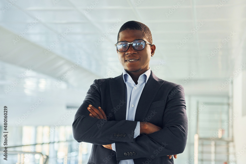 With arms crossed. Young african american businessman in black suit is indoors With arms crossed. Young african american businessman in black suit is indoors