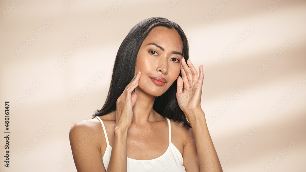 Female Beauty Portrait. Beautiful Asian Brunette Woman Posing, Smiling, Touching Her Face with Natural, Healthy Skin. Wellness and Skincare Concept on Soft Isolated Background. Close Up. Female Beauty Portrait. Beautiful Asian Brunette Woman Posing, Smiling, Touching Her Face with Natural, Healthy Skin. Wellness and Skincare Concept on Soft Isolated Background. Close Up.