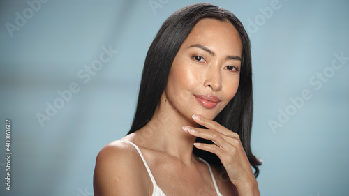 Female Beauty Portrait. Beautiful Diverse Asian Brunette Woman Posing, Smiling, Touching Her Face with Natural, Healthy Skin. Wellness and Skincare Concept on Soft Isolated Background. Close Up.