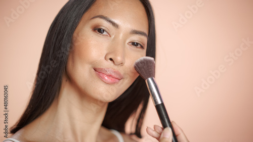 Female Beauty Portrait. Beautiful Happy Multiethnic Asian Brunette Woman Using Blush Makeup Brush in Wellness, Cosmetics, Spa and Natural Skincare Concept on Soft Isolated Background.