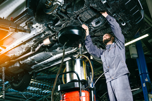 Engine oil change process. Used oil drain in lifted car. photo