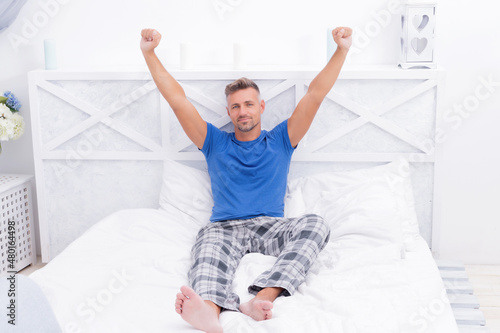 Happy man in pajamas wakeup stretching after sleep in bed, morning
