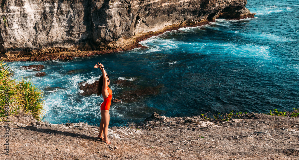A happy girl is resting at a sunny seaside resort. A beautiful girl in a red swimsuit on the seashore, panorama. A young woman enjoys a beautiful seascape on a paradise island in Indonesia. Copy space