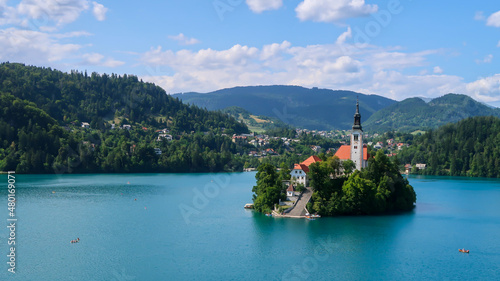 View of Catholic church situated on an island on Bled lake with mountains and villages on the background in the slovenian Alps