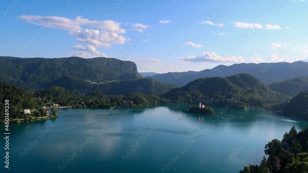 Panoramic view of Catholic church situated on an island on Bled lake with mountains and villages on the background in the slovenian Alps