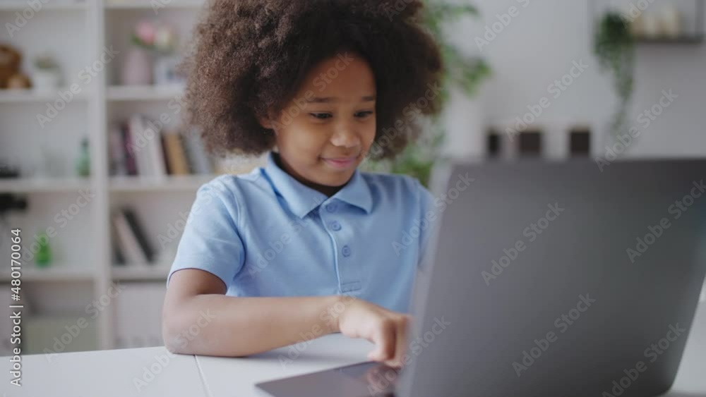 Smiling curly girl doing homework online, using laptop app, distance education Smiling curly girl doing homework online, using laptop app, distance education
