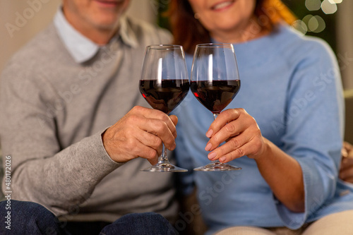 holidays, drinks and people concept - close up of happy smiling senior couple toasting glasses of red wine at home in evening