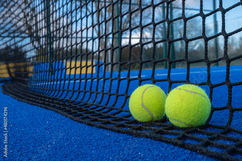 Two balls at the base of the net of a blue paddle tennis court © Vic