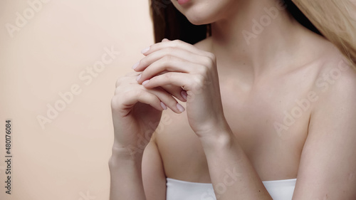 cropped view of young woman applying hand cream isolated on beige.