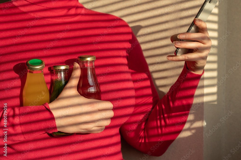 woman holding a phone and glass bottles with juices