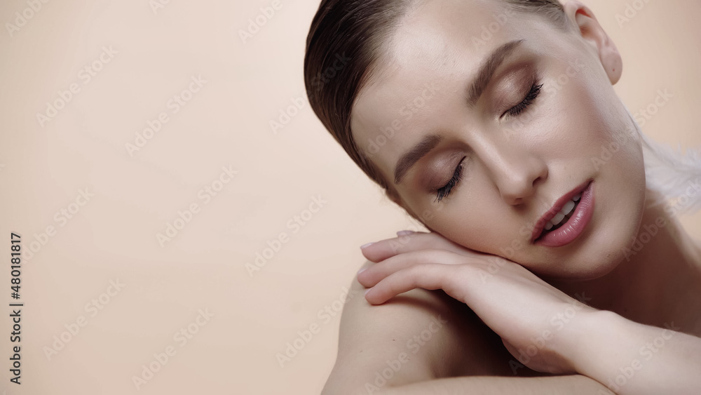 feather near cheek of young woman with closed eyes isolated on beige. feather near cheek of young woman with closed eyes isolated on beige.