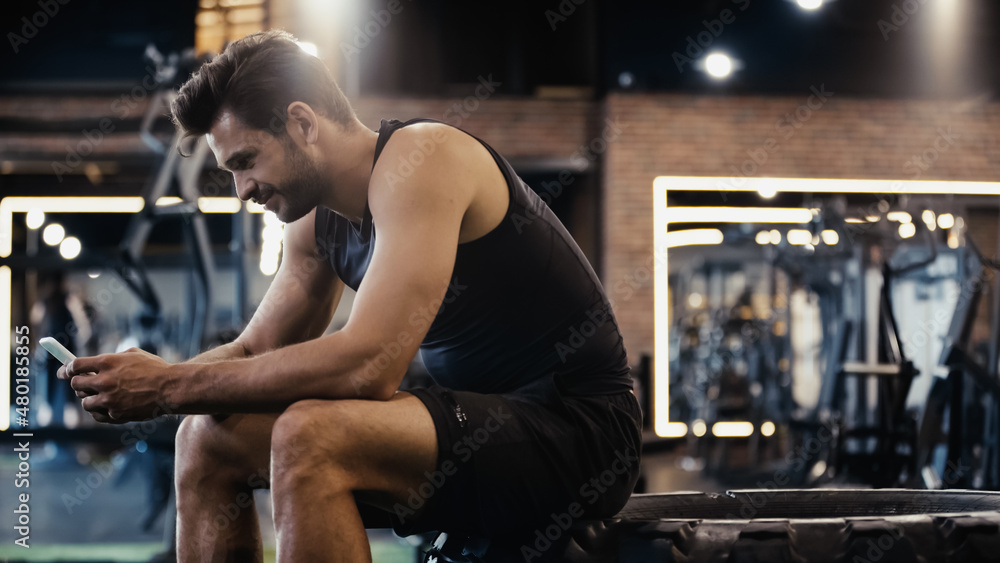 Fototapeta premium happy sportsman using smartphone while sitting on car tire.