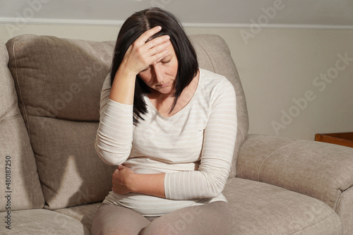  Middle aged mature pregnant woman suffering from headache and stomach ache, toxicosis at home. Abdominal pain, food poisoning, diarrhea, stomach ulcer, menstruation pain. photo