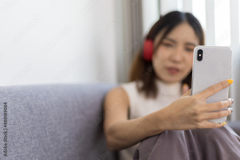 An Asian woman uses a cell phone to take a selfie on the sofa in the house. An Asian woman uses a cell phone to take a selfie on the sofa in the house.