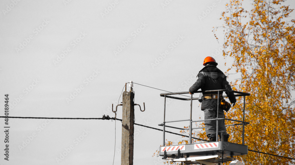 An electrician on a lift repairs an electric street pole