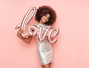 A beautiful young African-American woman with a balloon in the shape of the inscription love on a pink background. Woman on Valentine's Day. Symbol of love