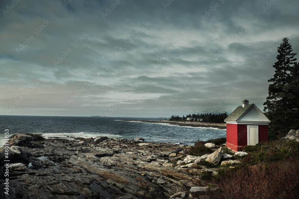 Rocky wild coast of the Atlantic Ocean. USA. Maine. A small lighthouse house on the rocks by the water.