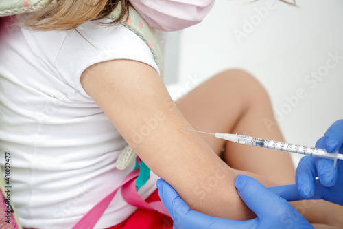 Criança sendo vacinada contra covid 19 volta as aulas medica com luva azul e seringa.
 photo