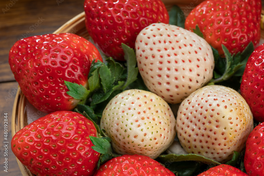 Red and white strawberries in a wooden basket on wooden background, Red Strawberry and Pine berry or Hula strawberry in Bamboo basket.