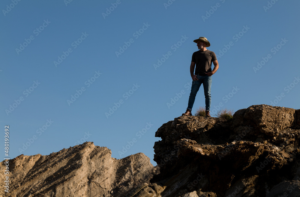 Adult man in cowboy hat standing on top of cliff in Tabernas Desert, Almeria, Spain