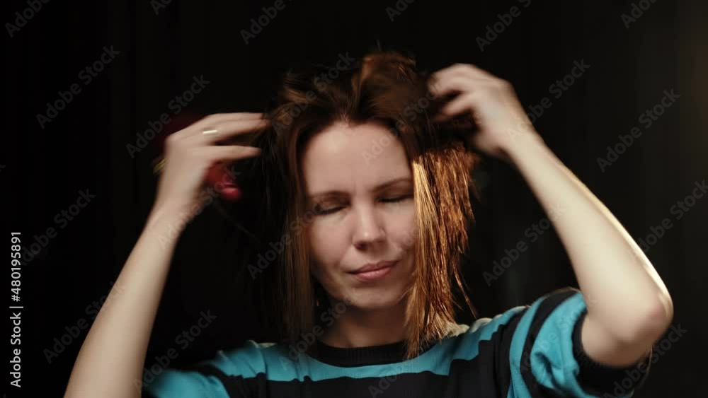 A middle-aged woman is combing her hair with a comb. A forty-year-old woman. Hair care. Dark background. A middle-aged woman is combing her hair with a comb. A forty-year-old woman. Hair care. Dark background.