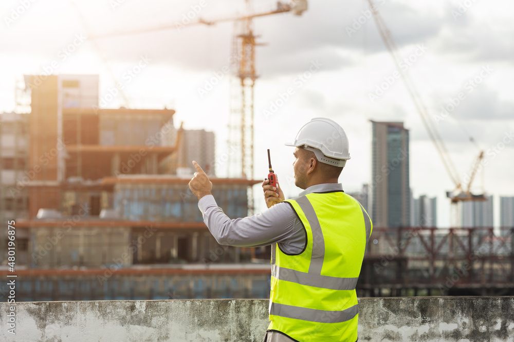 © Chanakon - Asian engineer handsome man or architect use radio communication with white safety helmet in city construction site . Standing on rooftop building construction at capital.