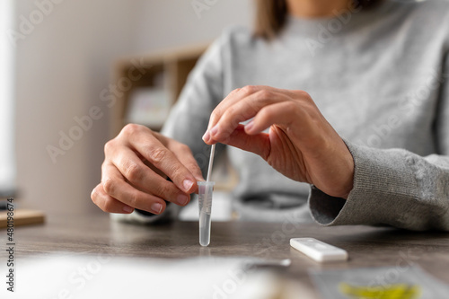 medicine, quarantine and pandemic concept - hands of woman making self testing coronavirus test and stirring swab in reagent at home