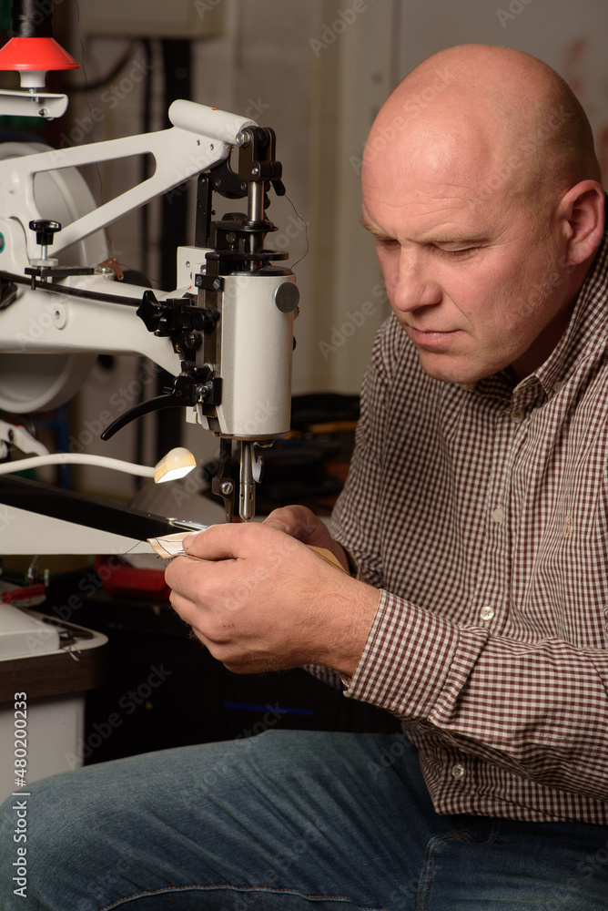 Shoemaker stitching on industrial sewing machine in workshop. Concentrated man setting up sewing machine on factory. Footwear and clothes manufacturing industry concept.